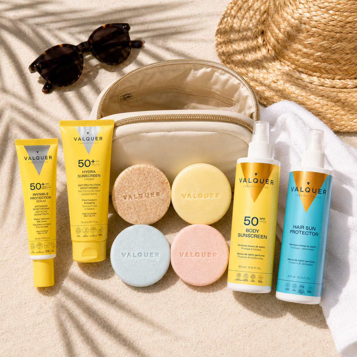 Protectores solares faciales, corporal y capilar junto a cosmética sólida Valquer en un neceser de viaje sobre la arena.